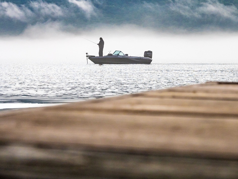 View from a dock of a man in a boat on the water while fishing, angling for beginners concept. 
