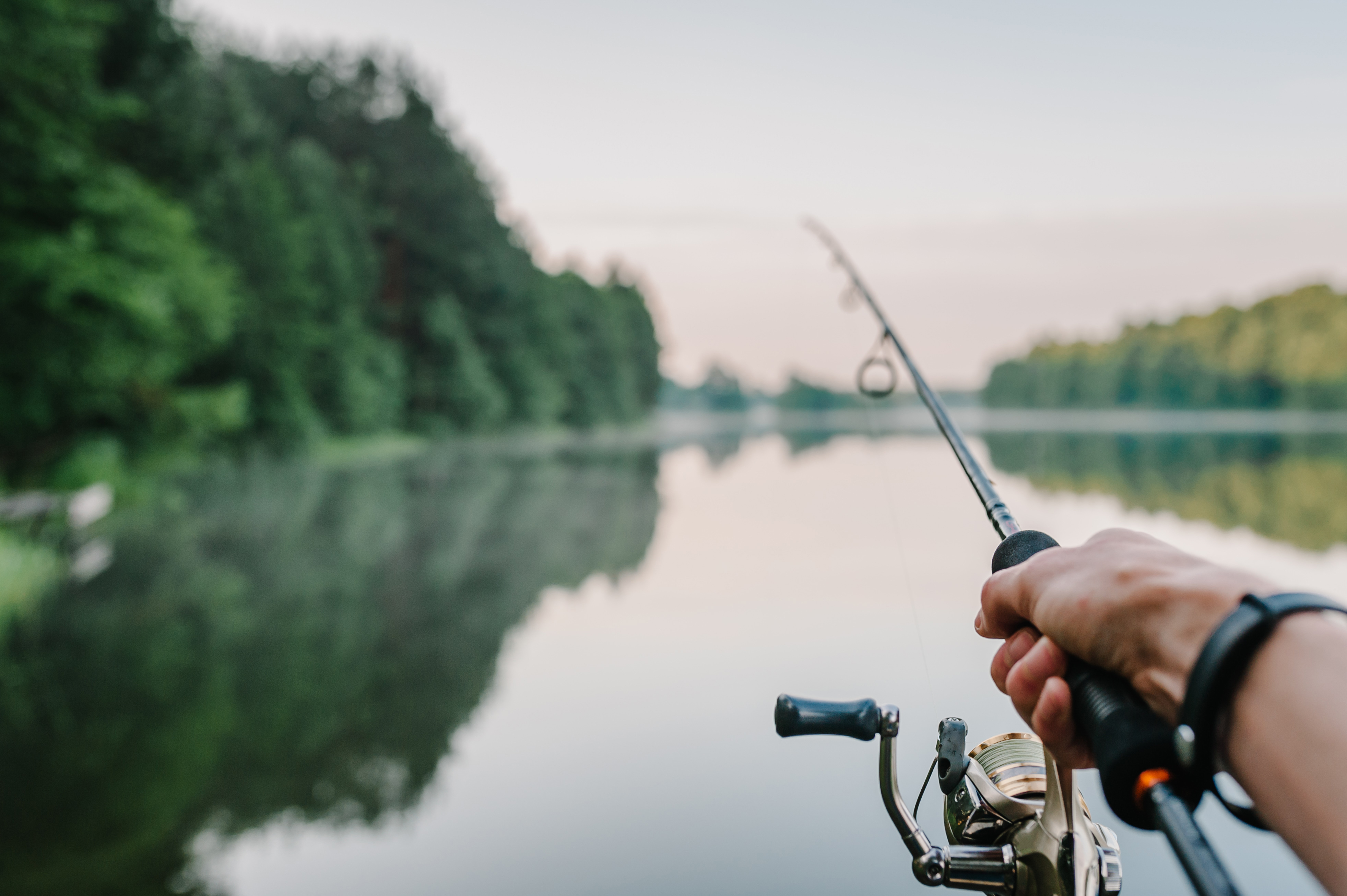 Close-up of a hand holding a rod and reel while fishing in a boat, boat safety concept. 