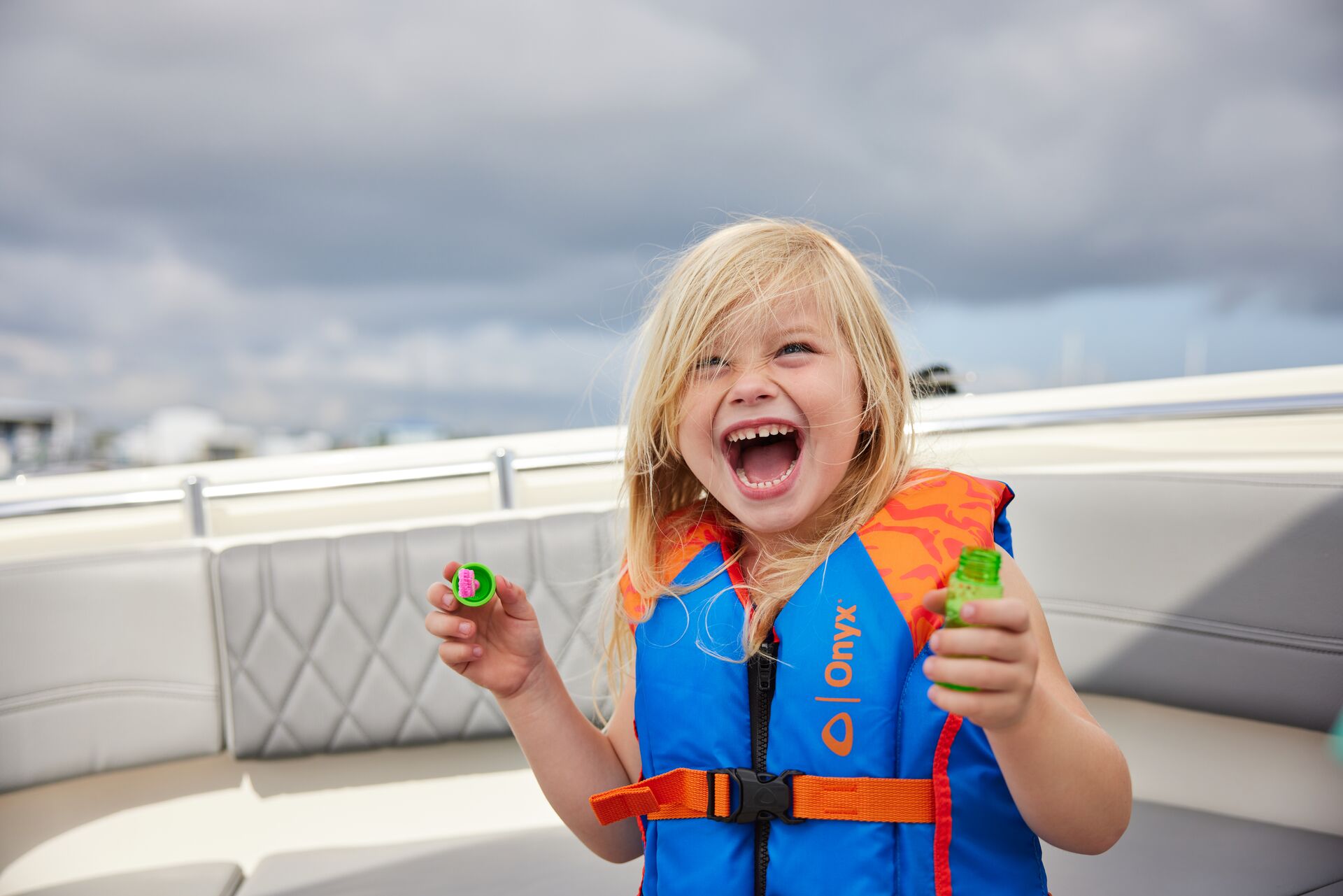 Small girl in a life jacket blowing bubbles on boat. 