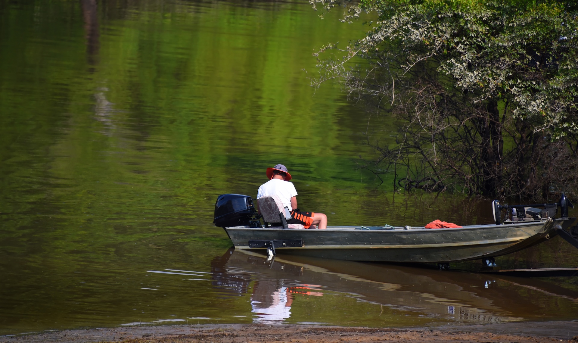 Man in a flat bottom boat near shore.