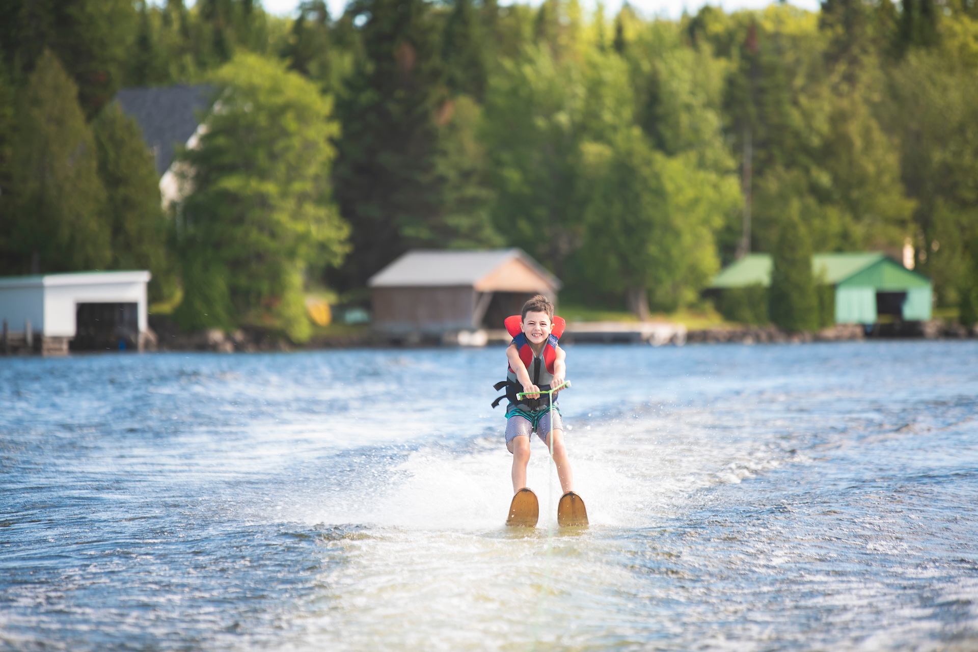 Kid on water skis smiling and wearing a life jacket. 