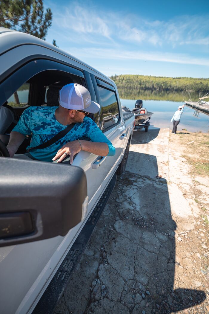Man in truck looks back while backing trailer and boat into water.