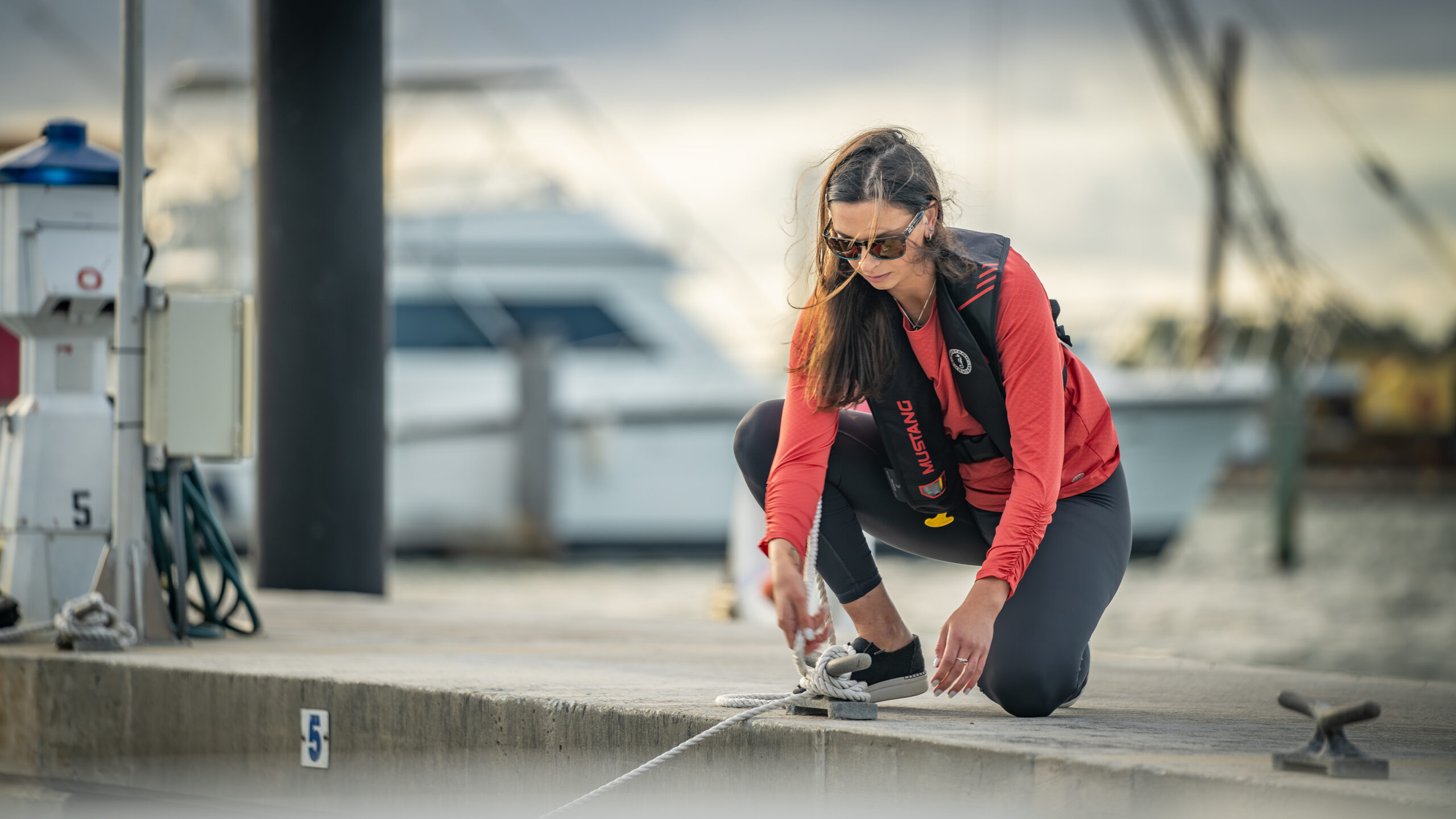 Woman at dock tying rope wearing inflatable life jacket. 