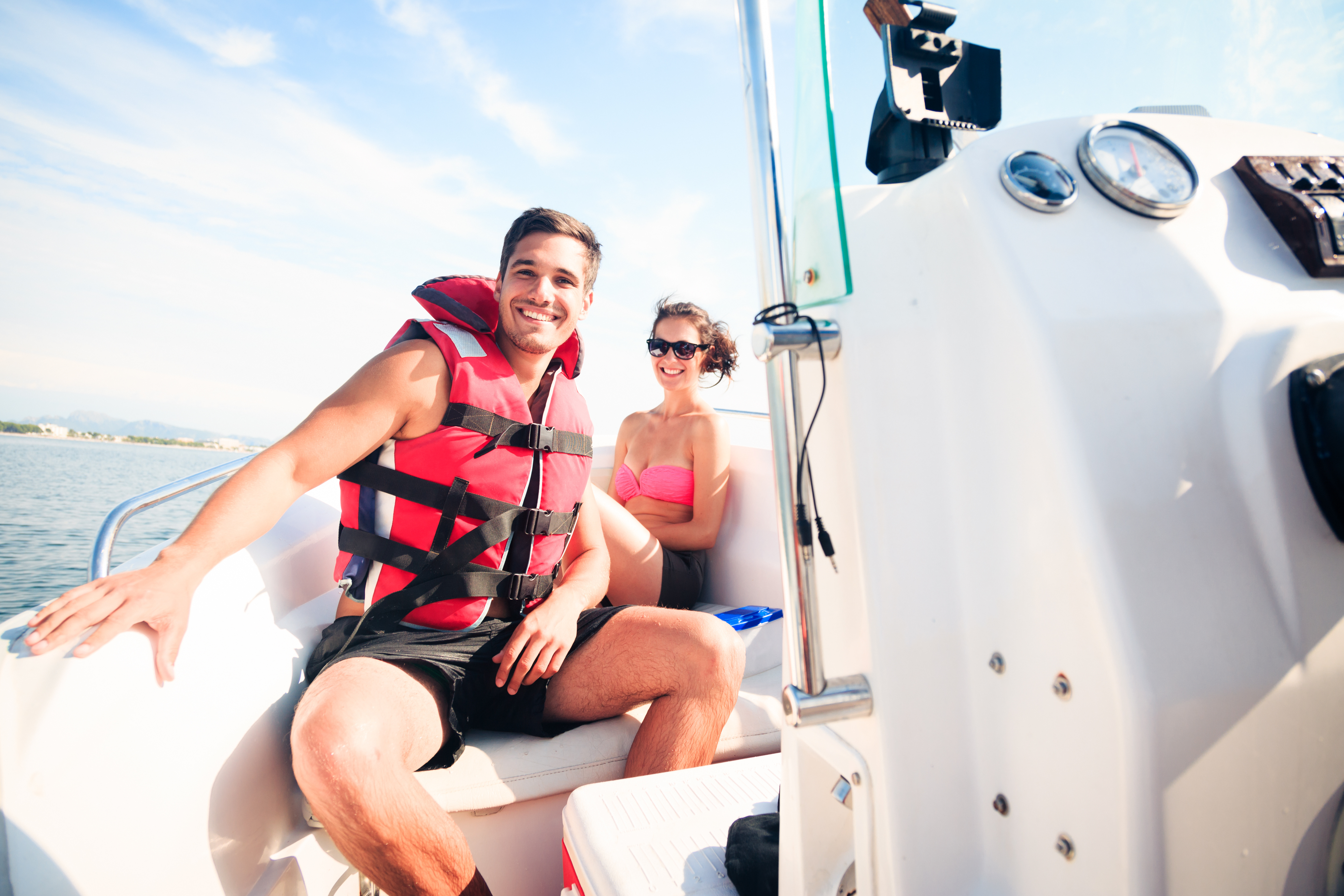 A man and woman on a boat wearing life jackets, safe boating season concept.