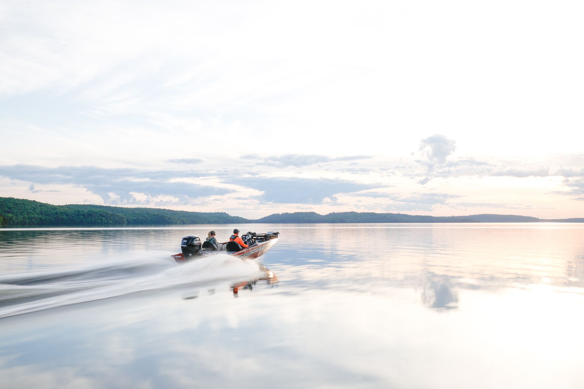 Two people on fishing boat riding across lake. 