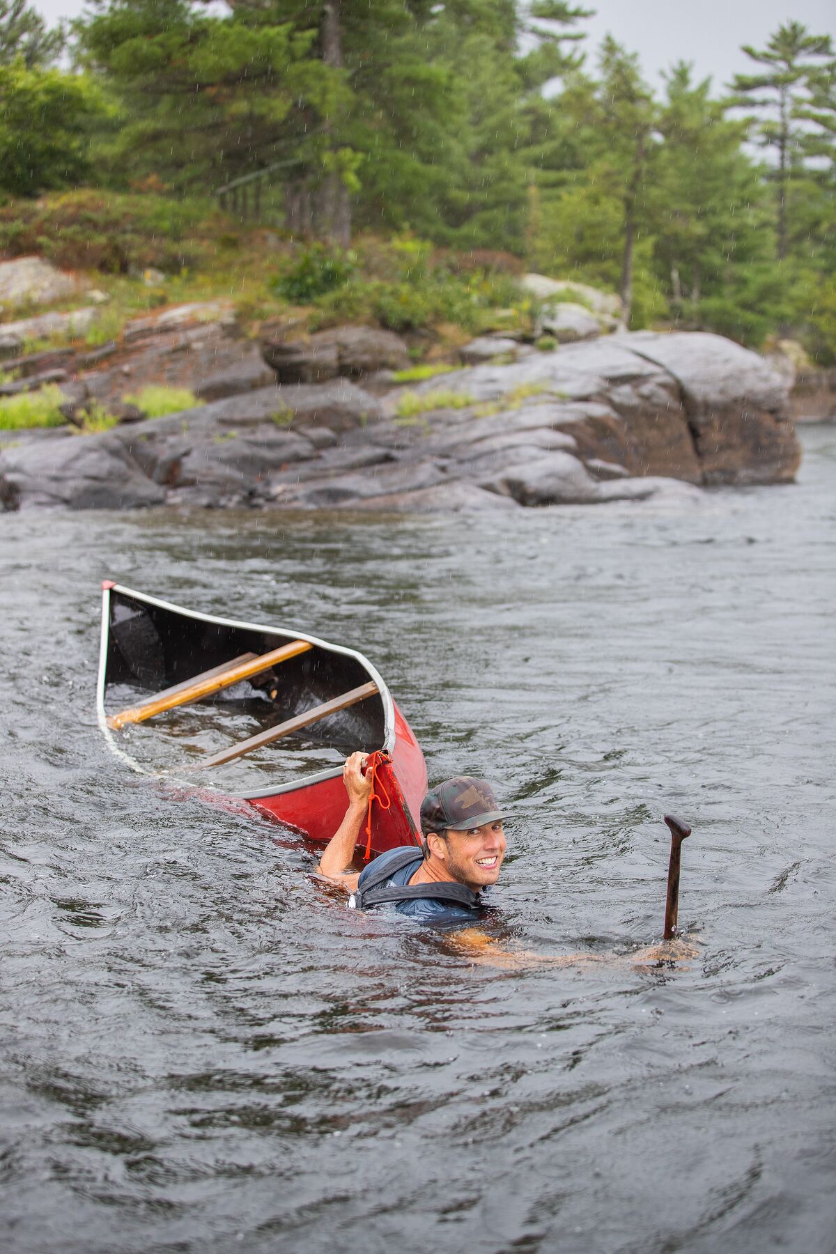 Guy in river with overturned canoe, upstream vs downstream dangers concept.