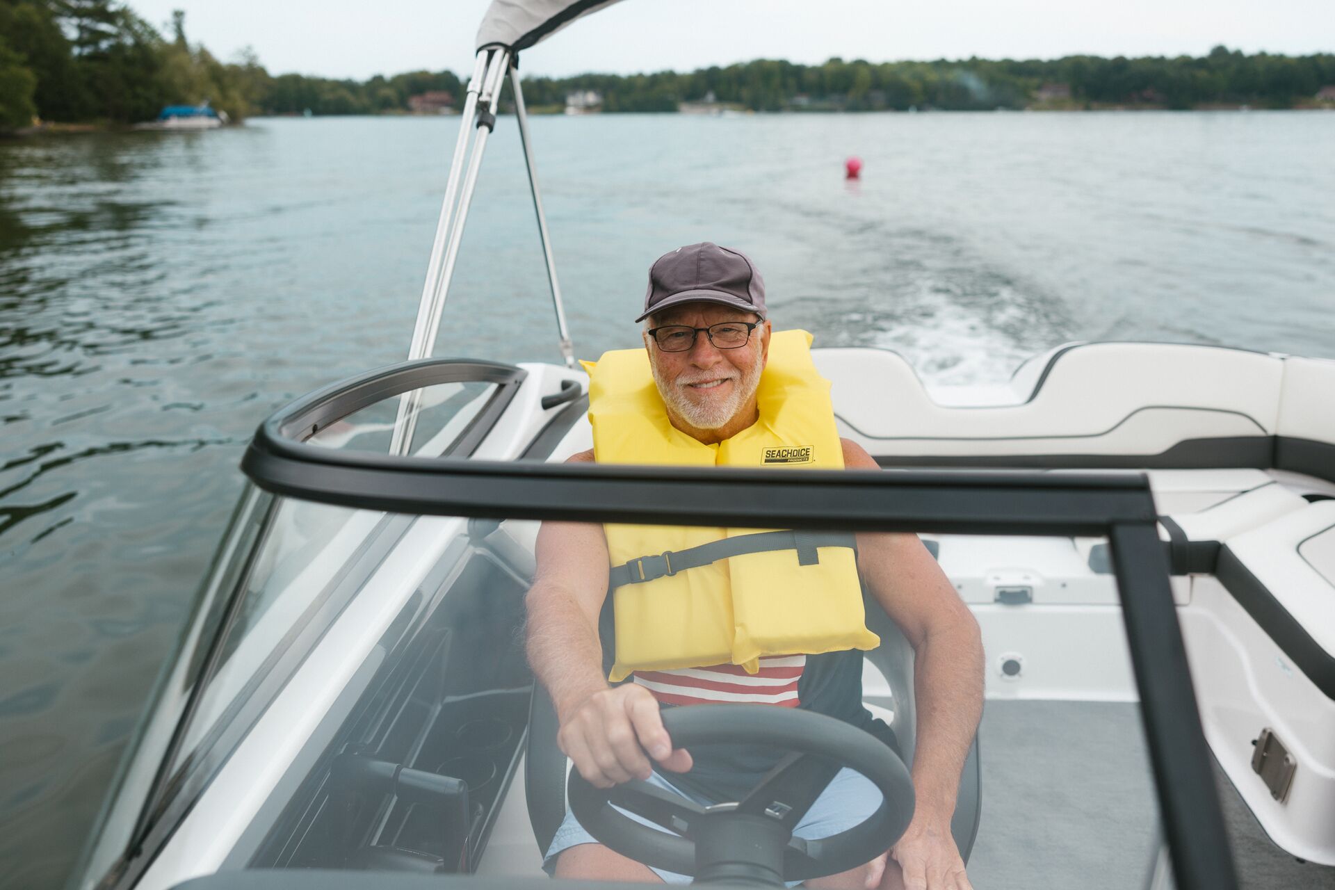 Smiling man in yellow life jacket drives boat on lake. 