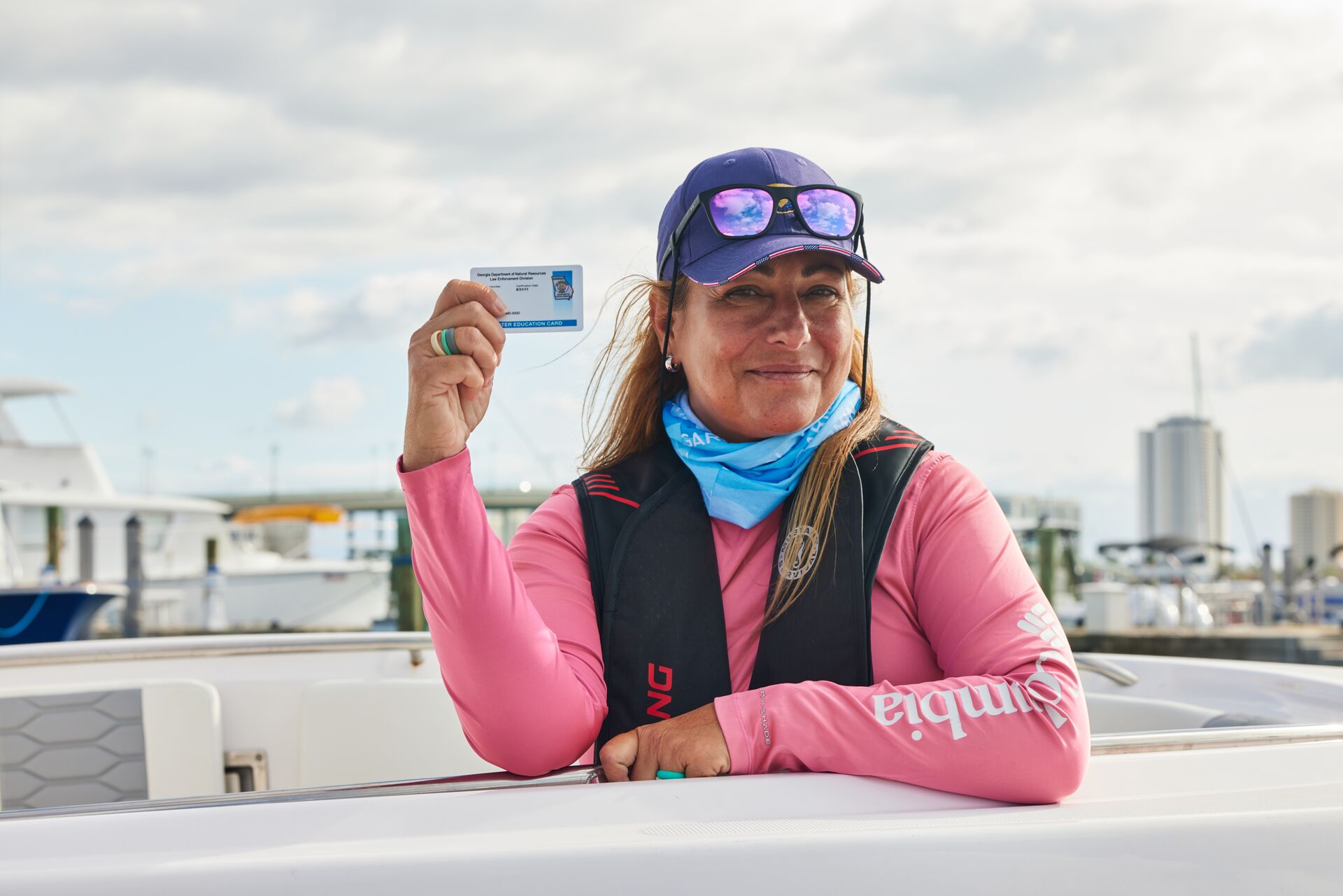 Woman wearing hat and life jacket holds boater card, take Missouri boaters ed concept. 