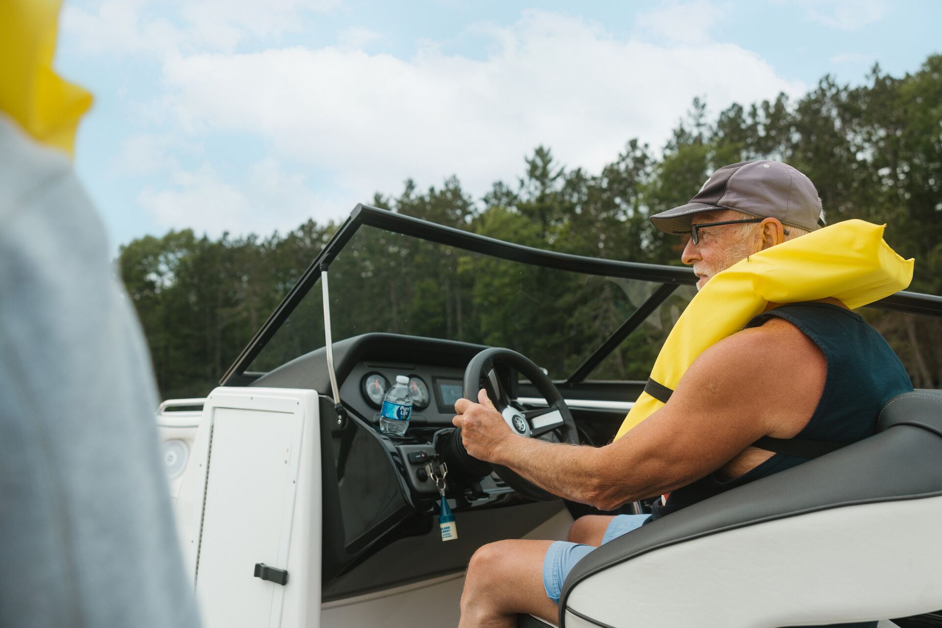 Man smiles and drives boat while wearing yellow life vest, get an Arizona boating license concept.