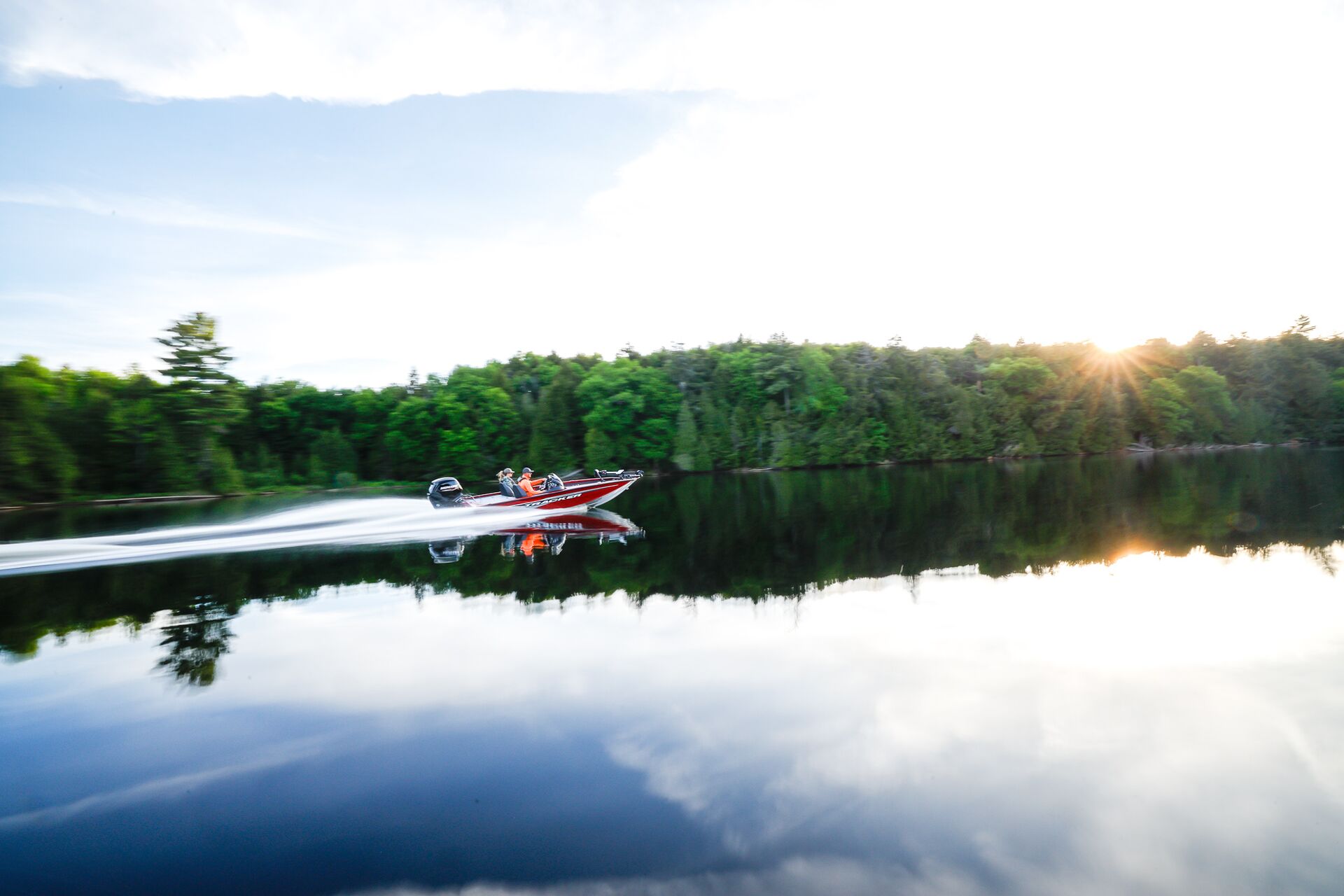 Red boat moves along tree-lined lake shore, do you need a boating license in Missouri concept. 