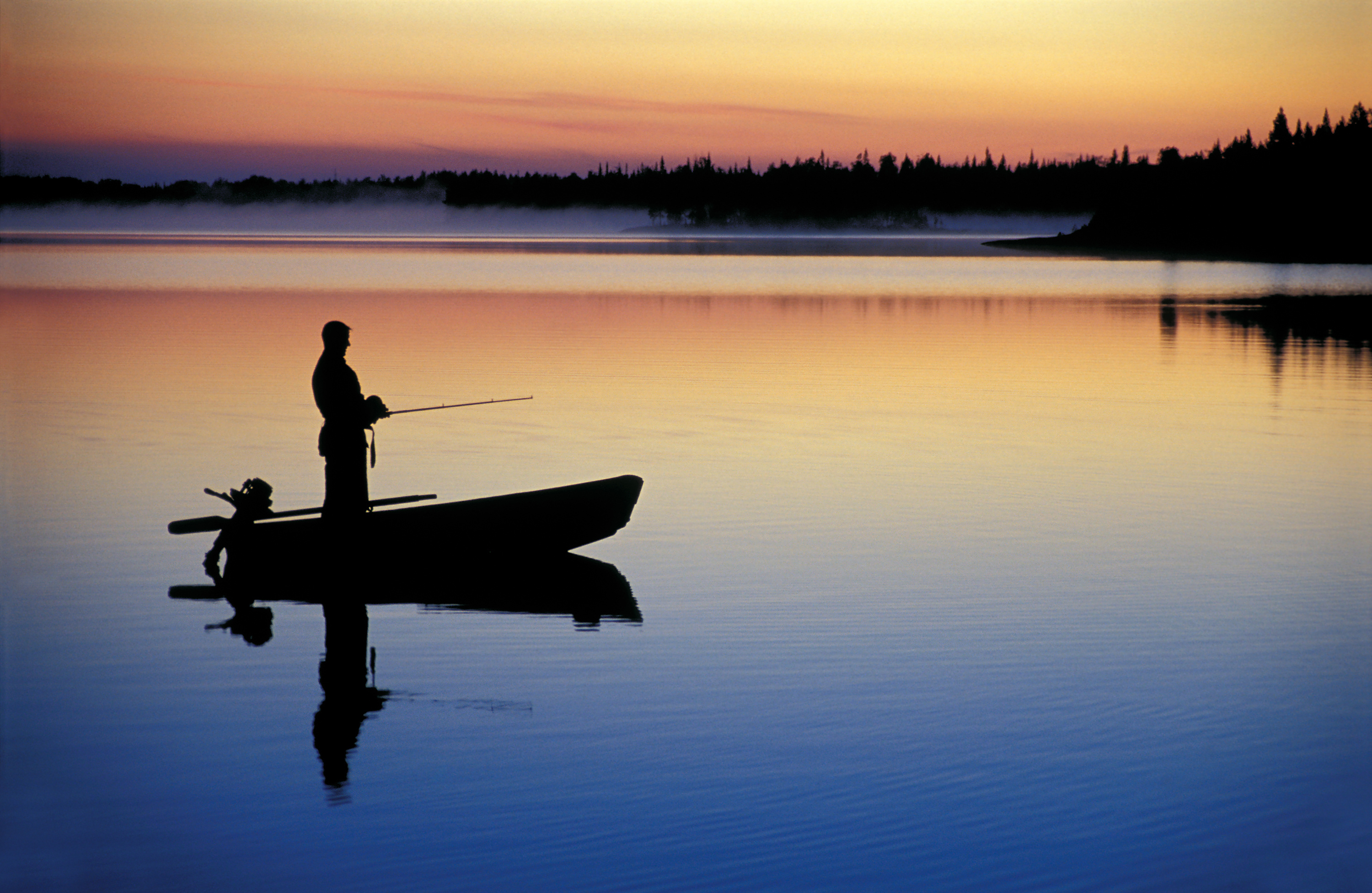 Silhouette of a person fishing from a small boat on a lake. 