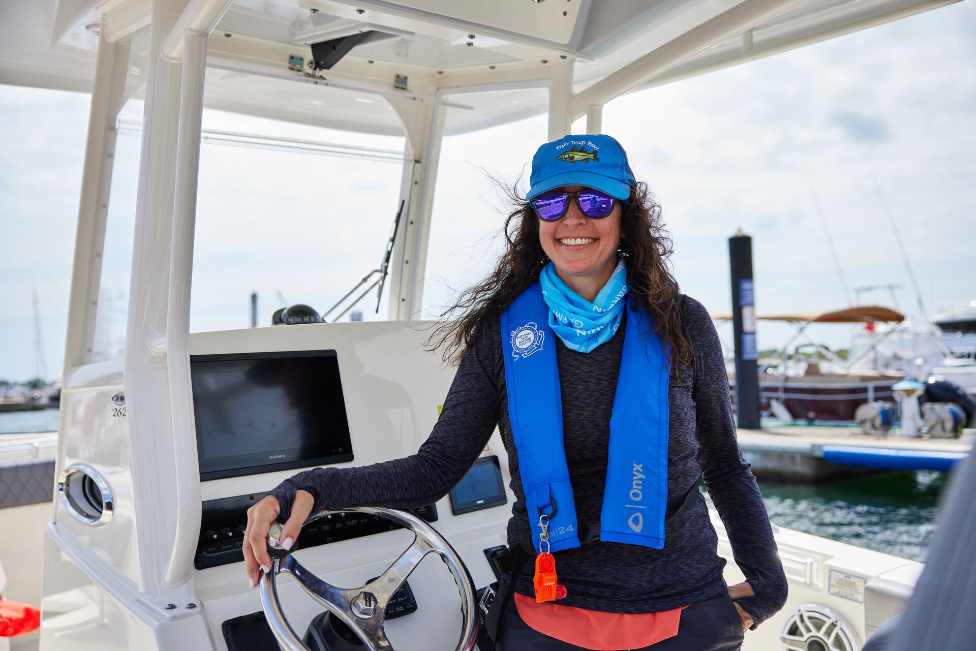 Smiling woman in blue life jacket at the helm of a boat. 