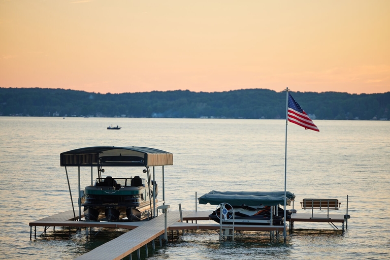 A pontoon boat at a dock out of the water with a U.S. flag flying nearby.