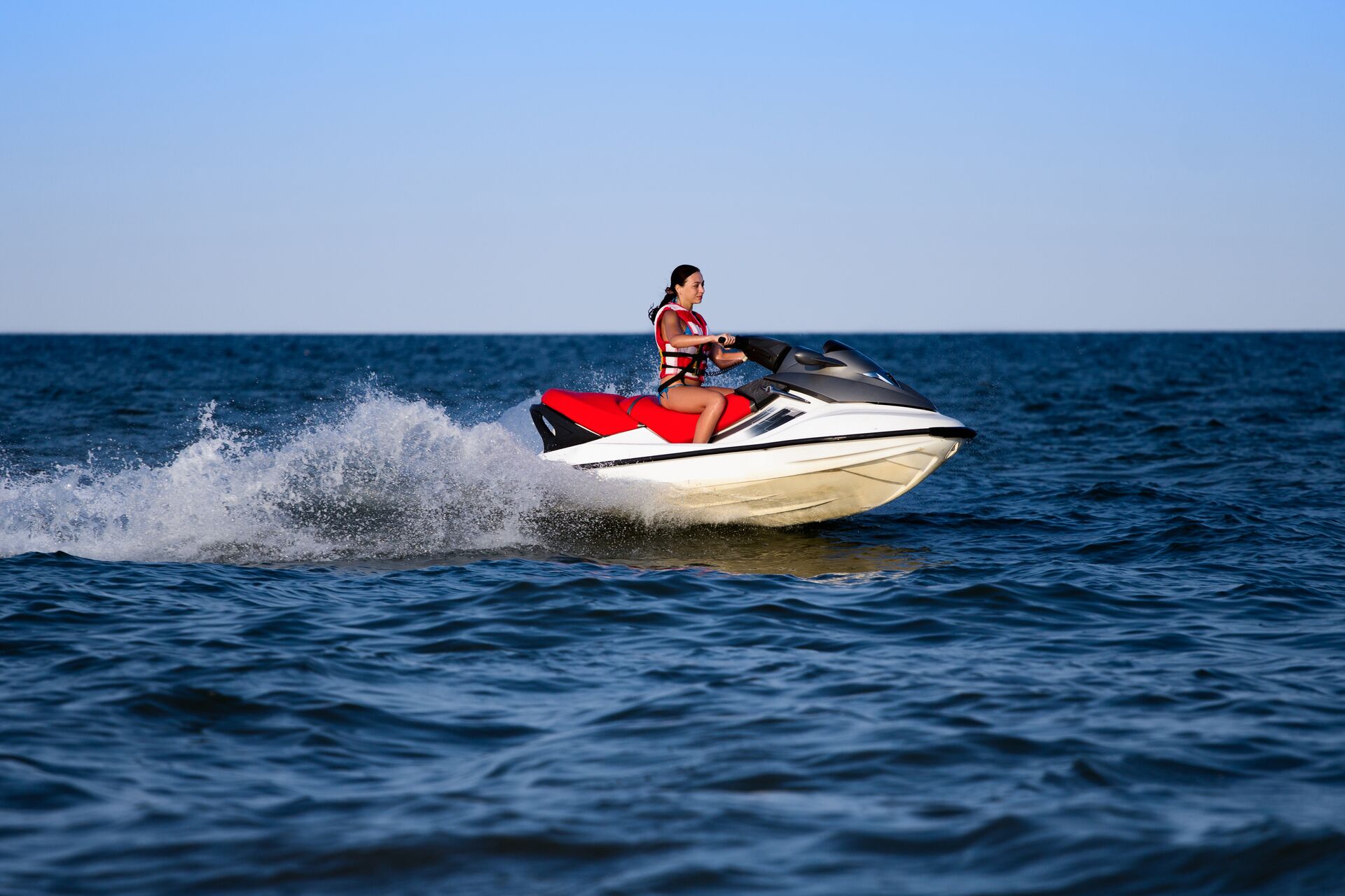 Girl wears life jacket while driving jet ski.