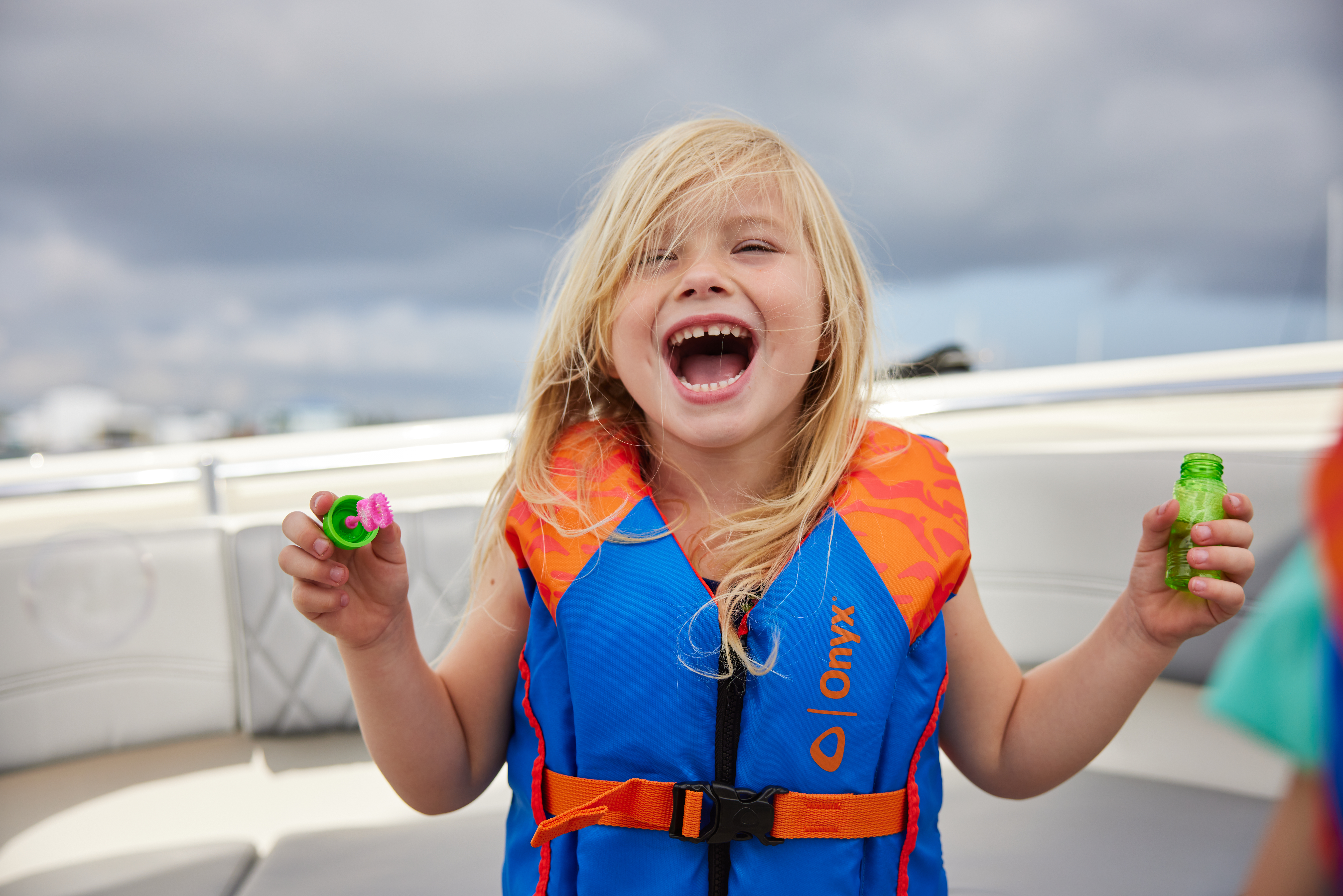 A young girl wearing a life jacket and blowing bubbles on a boat, July 4th Weekend concept. 