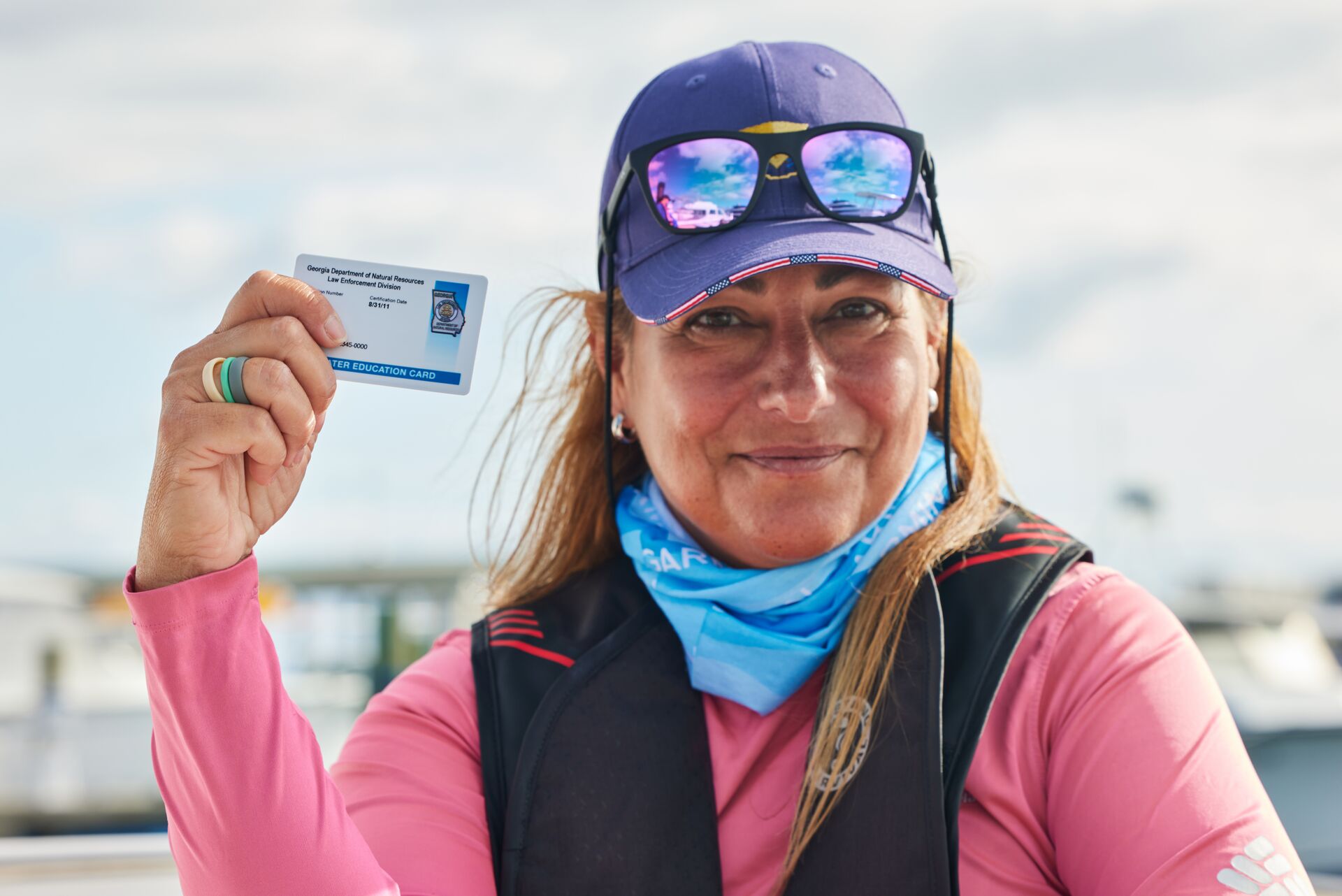 Smiling woman in life jacket holds boater card, Boat-Ed vs BoatUS foundation concept.
