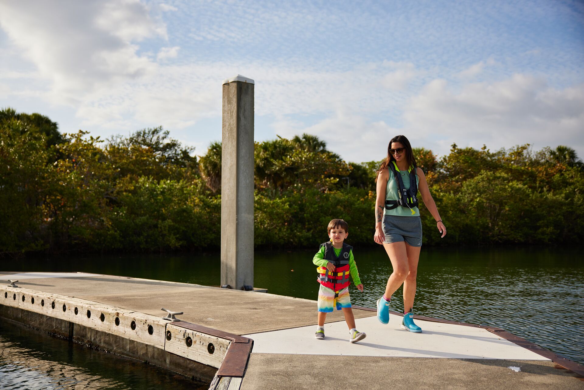 Woman and child wear lifejackets on dock, boating safety checklist concept.
