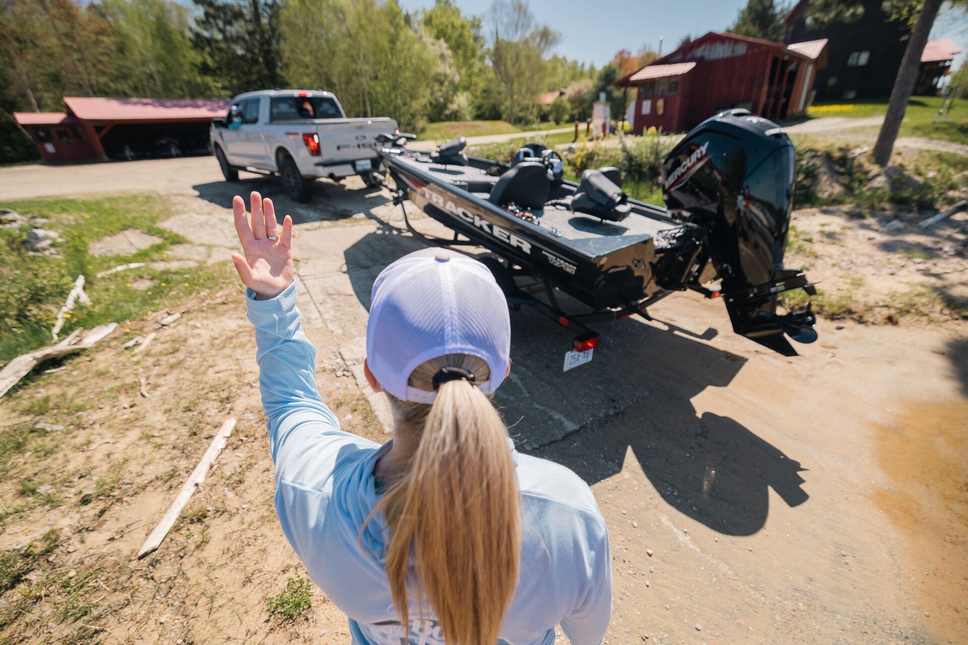 Woman signals to truck backing boat on trailer down ramp, summer boating safety tips concept.
