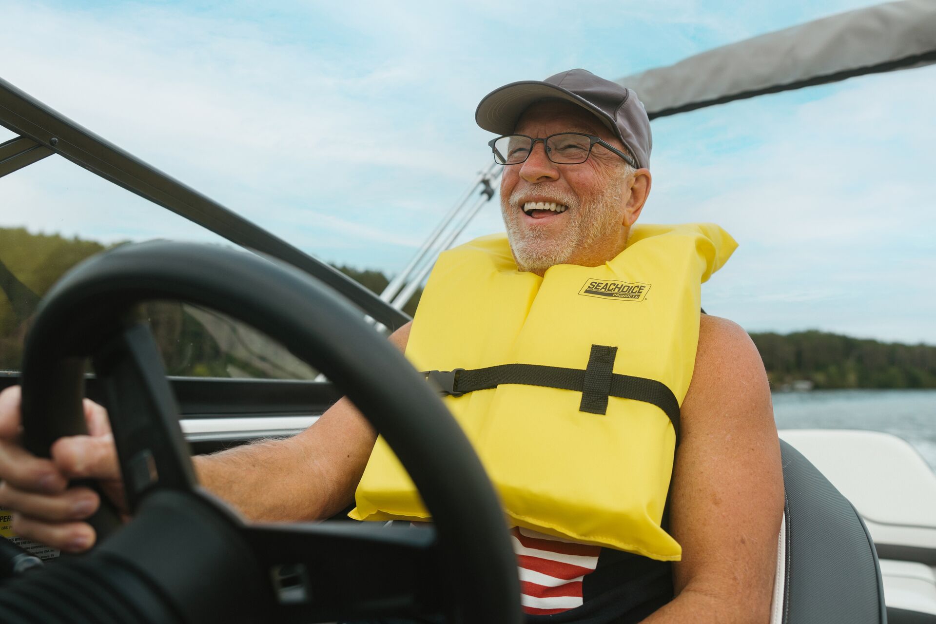 Man at boat helm wears life jacket and smiles, pass a boater safety course concept. 