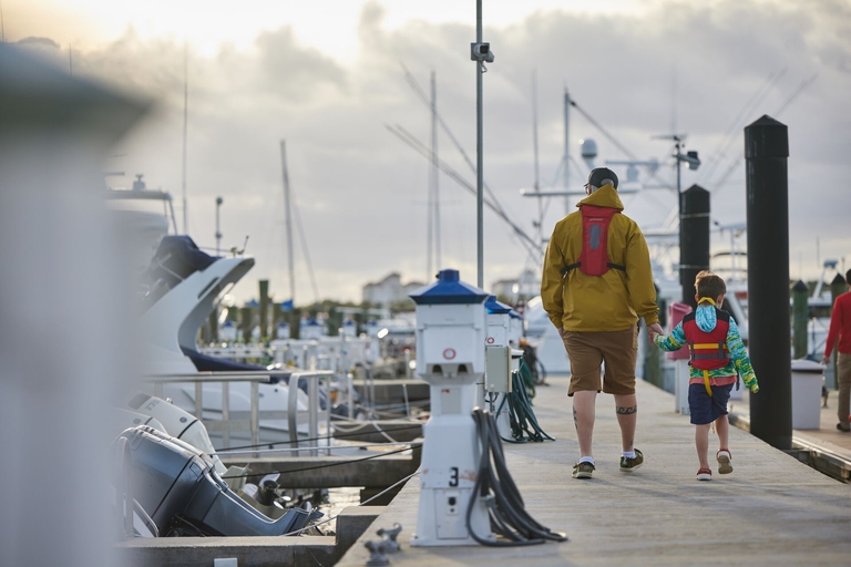 Man and boy in lifejackets walk on dock, lifejacket maintenance concept.