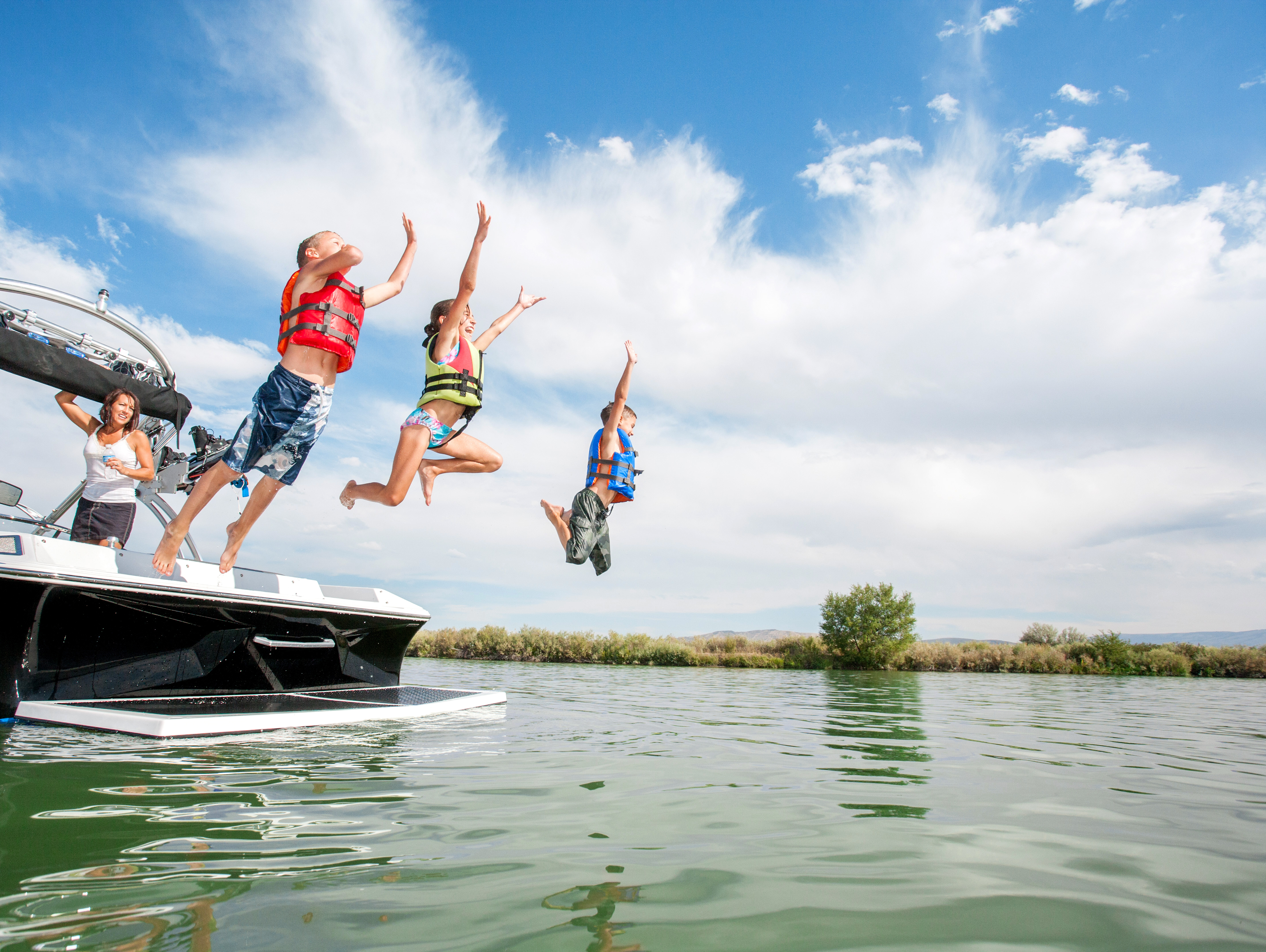 Kids wearing lifejackets jumping in the water from a boat. 