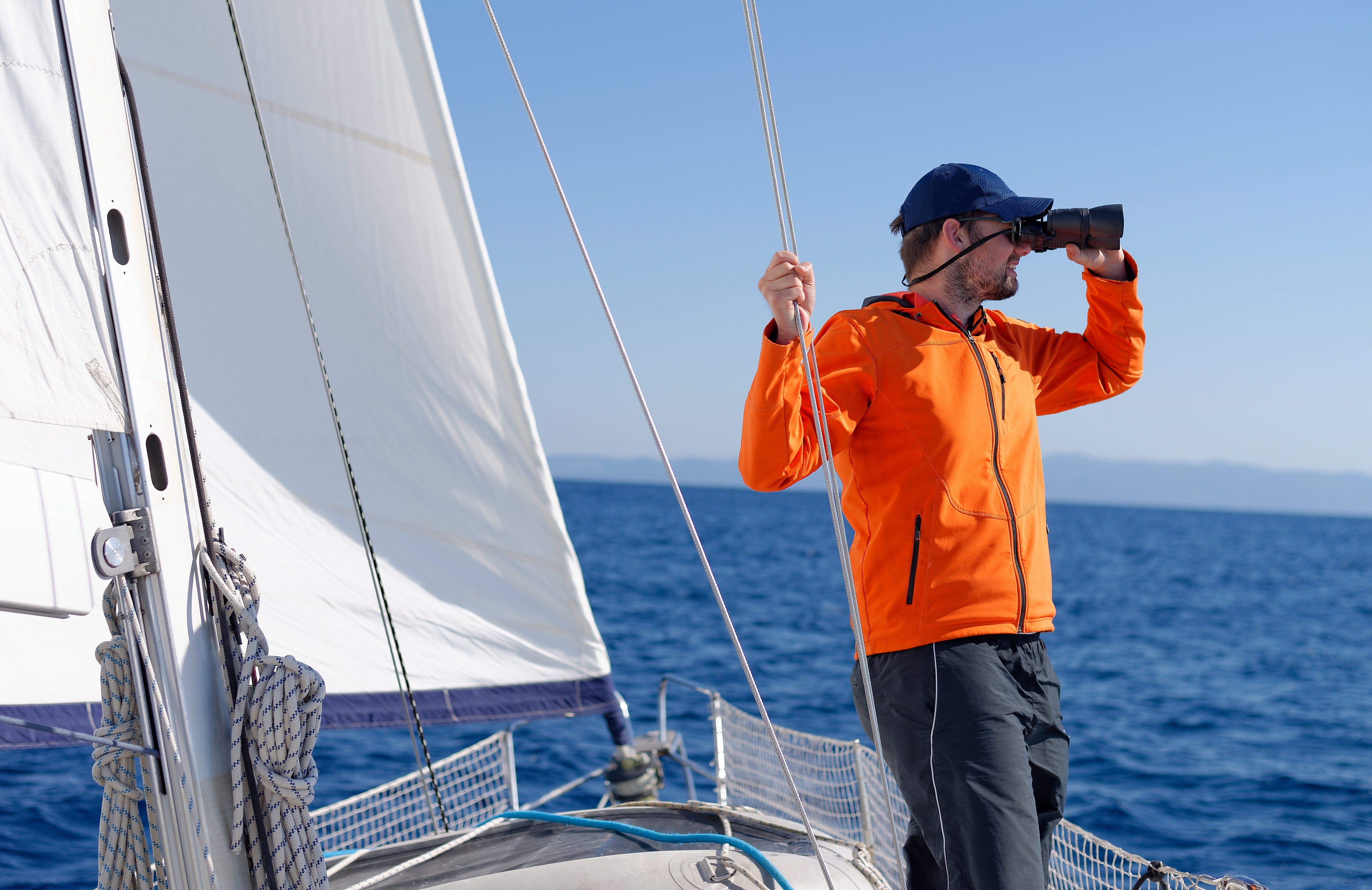 A man on a sailboat using bincoulars, safety on sailboats concept.