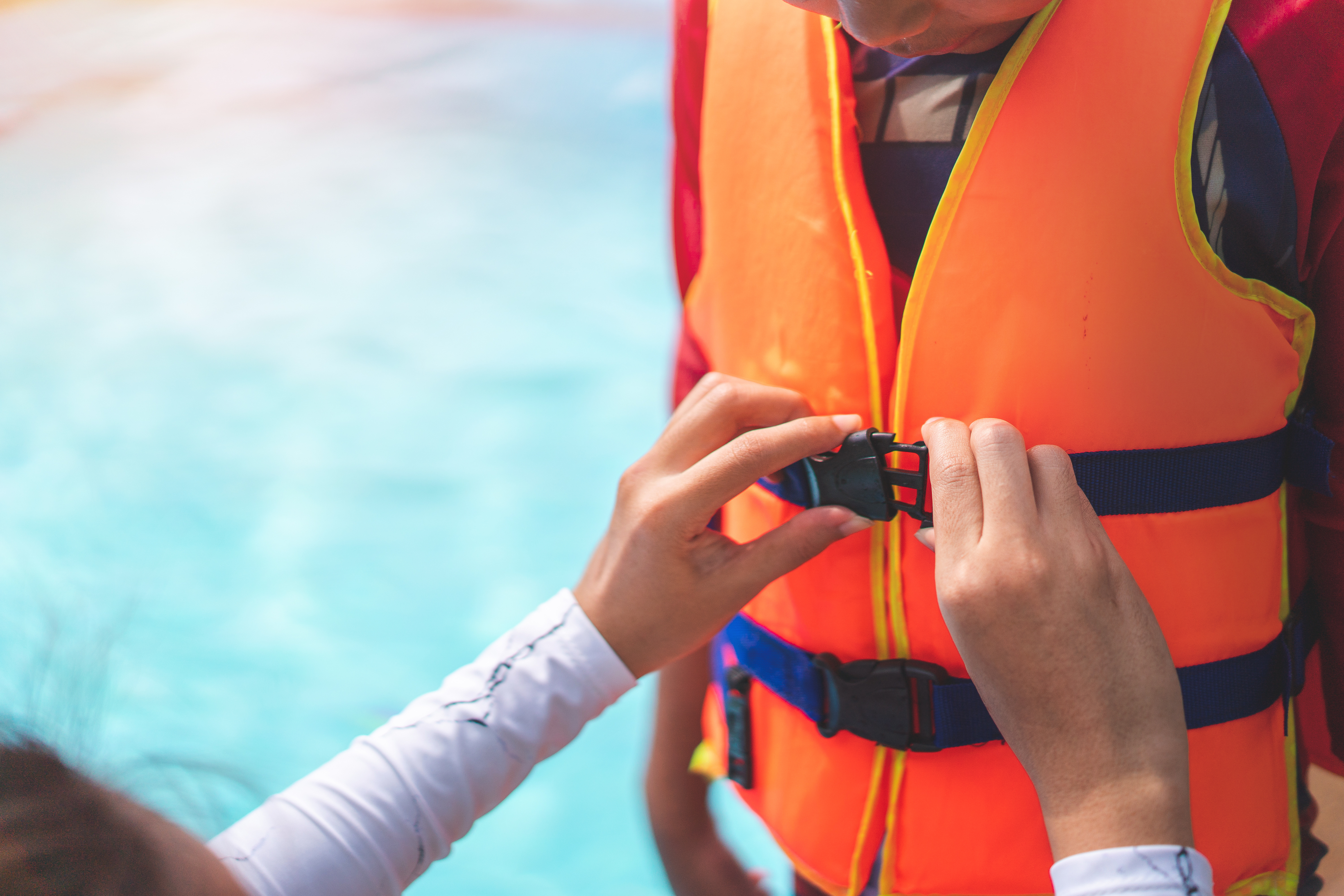 A person helping a child wear a PFD life jacket. 