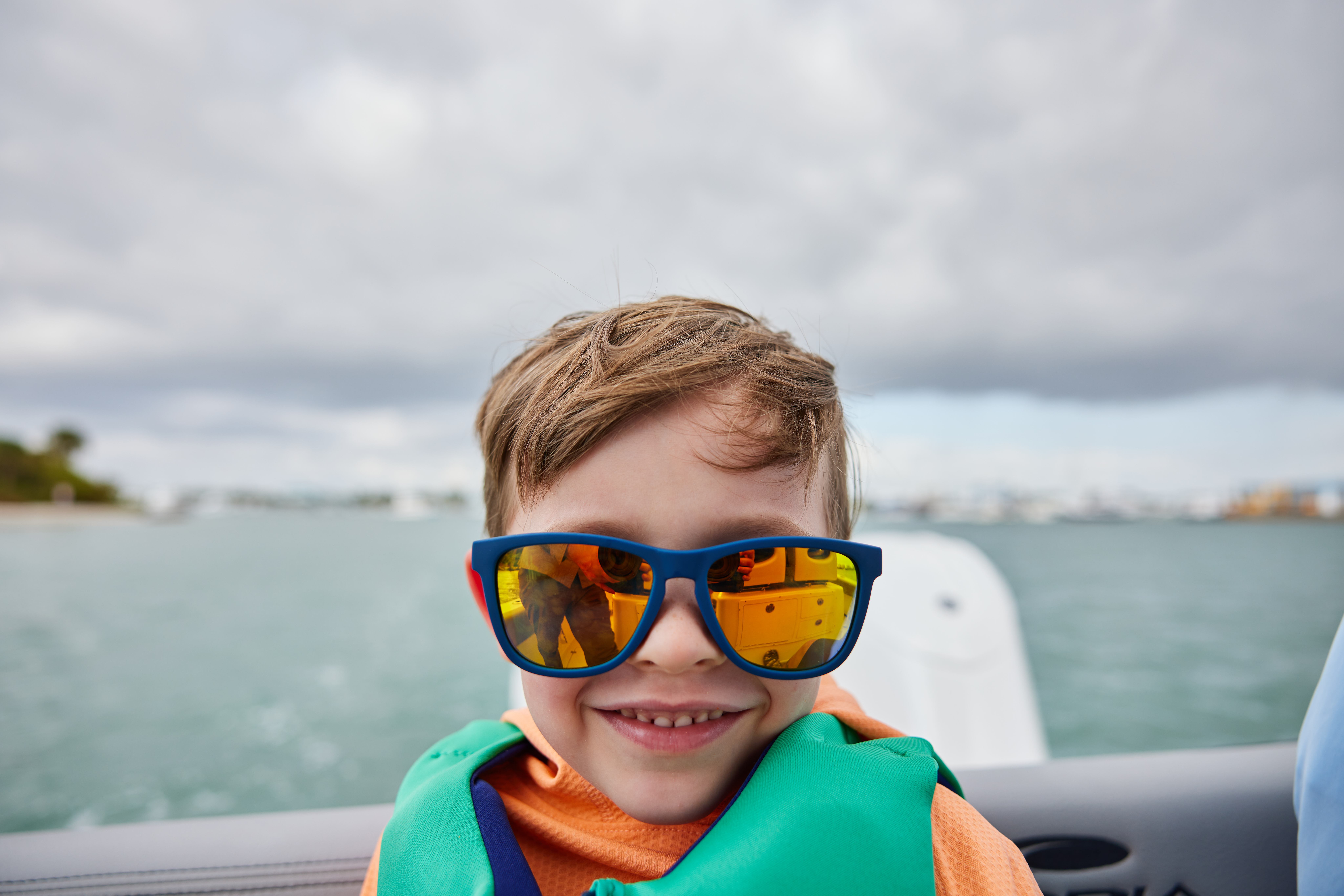 A child wearing sunglasses and a lifejacket on a boat, what is a pontoon boat concept. 