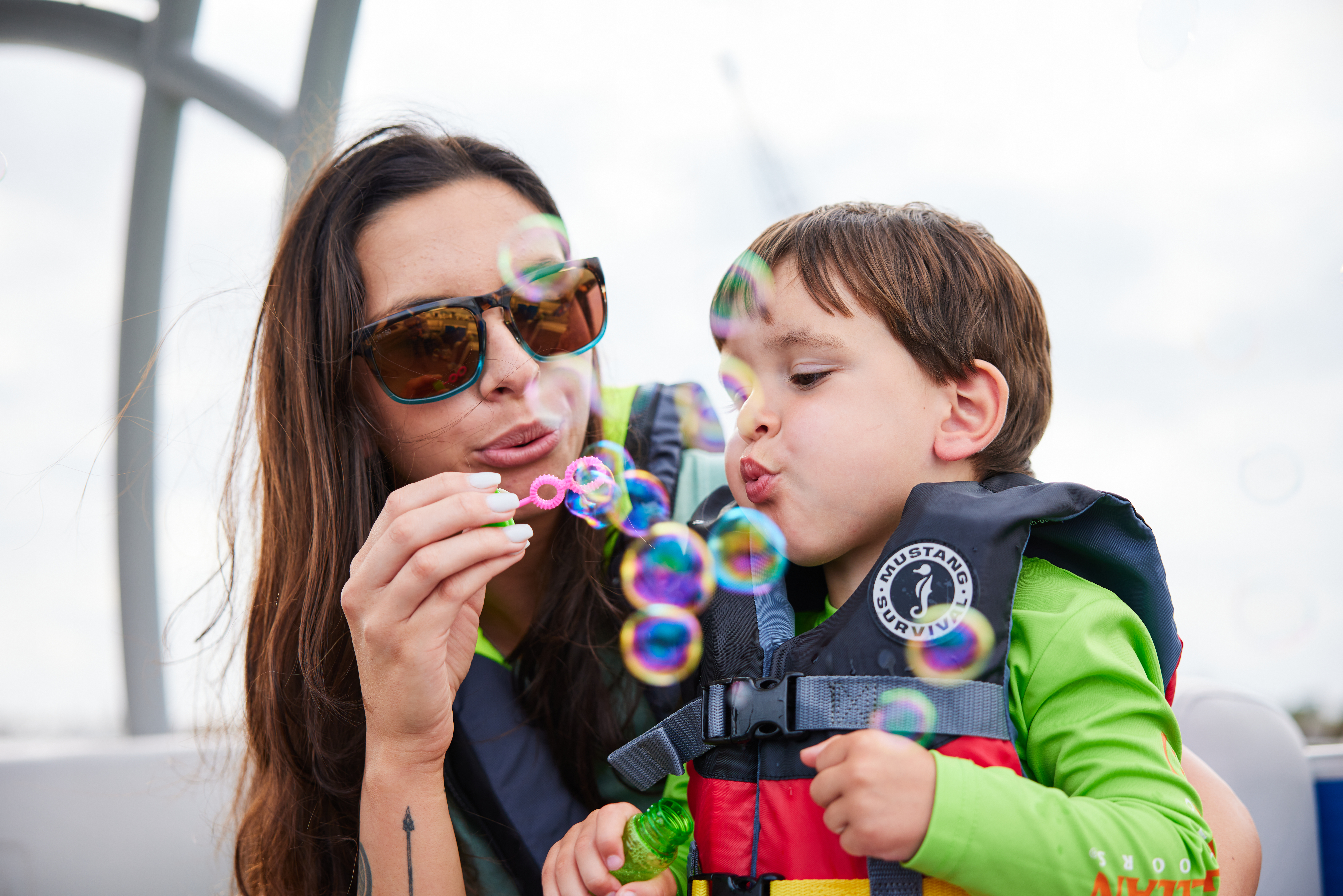 A woman and child blow bubbles while wearing lifejackets, pontoon boat concept. 