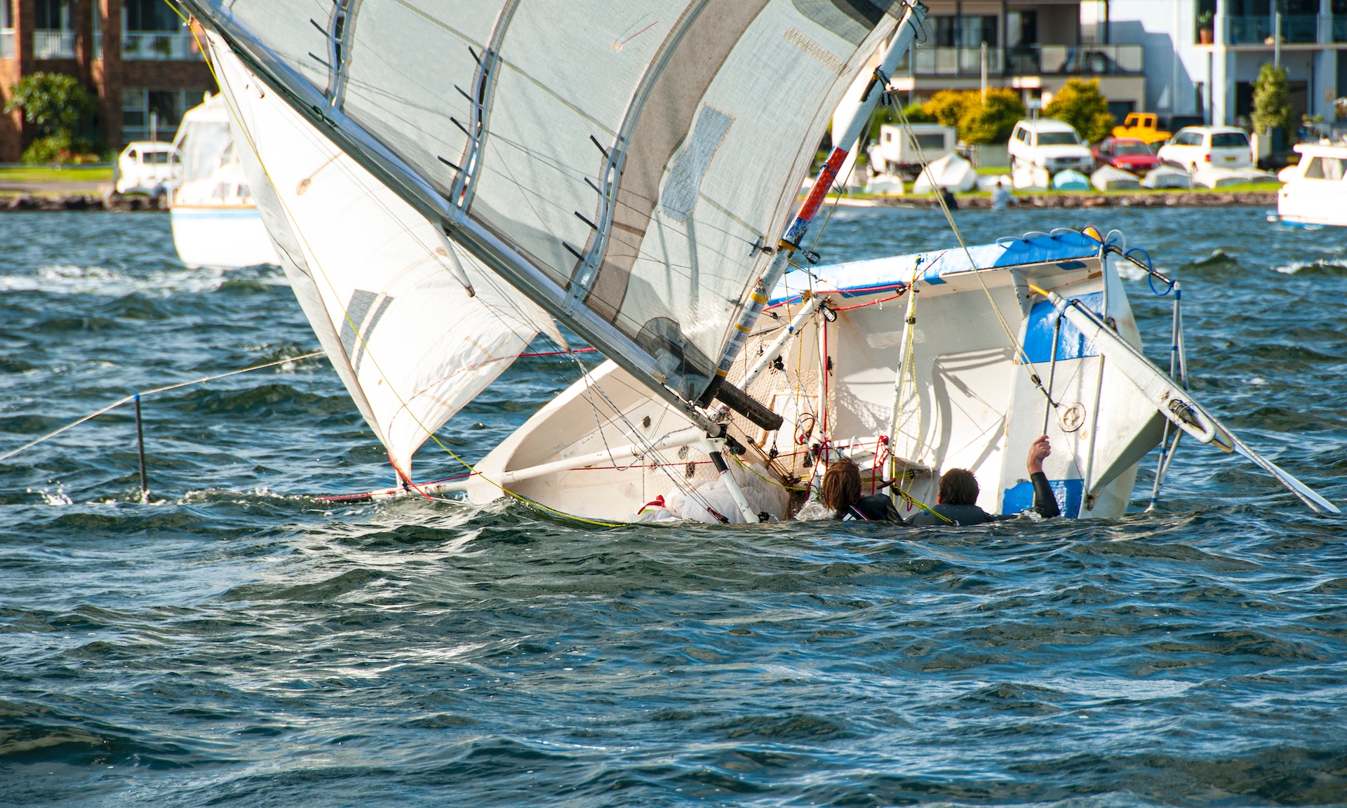 People hanging on to sailboat as it capsizes. 